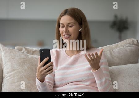 Une jeune femme dans des écouteurs ayant une réunion virtuelle utilise une application mobile Banque D'Images