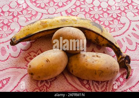 Un plantain et trois pommes de terre blanches sont sur une table recouverte de dentelle rouge et blanche. Banque D'Images
