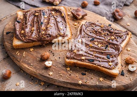 Planche de pain avec pâte de chocolat et bonbons de fête saupoudrer et noisettes sur fond de bois. Nourriture populaire de dessicer. Vue de dessus. Banque D'Images