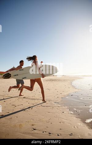 Un jeune couple de surfeurs court le long de la côte avec leurs planches de surf. Banque D'Images