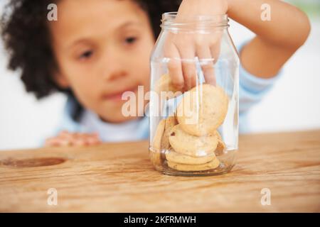 MMM, tellement de cookies juste pour moi. Un jeune garçon mignon saisissant un cookie du pot à biscuits. Banque D'Images