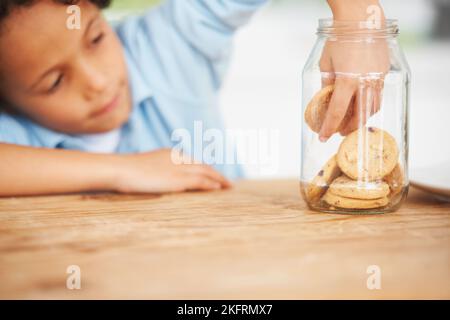 MMM, tellement de cookies juste pour moi. Un jeune garçon mignon saisissant un cookie du pot à biscuits. Banque D'Images