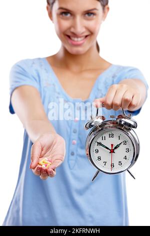 Revenez en arrière avec les vitamines du jour. Studio portrait d'une jeune femme tenant une poignée de comprimés et une horloge. Banque D'Images