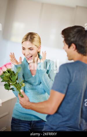 Laissez vos fleurs parler. Un jeune homme affectueux donnant à sa belle jeune femme un bouquet de roses roses. Banque D'Images