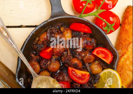 Seiches bébé rôti sur iron skillet avec les tomates et les oignons sur table en bois rustique Banque D'Images