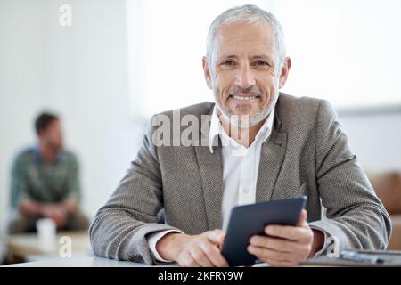 Cette tablette me facilite la vie. Portrait d'un homme d'affaires mature assis à une table dans un bureau. Banque D'Images