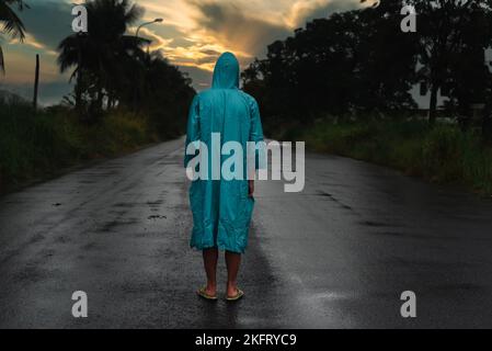 Concept dépressif avec homme seul en imperméable debout sur route humide sous la pluie au coucher du soleil Banque D'Images