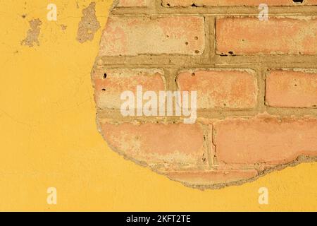 Texture. Sur le mur laqué jaune, une partie du plâtre s'écroule en brique. Banque D'Images