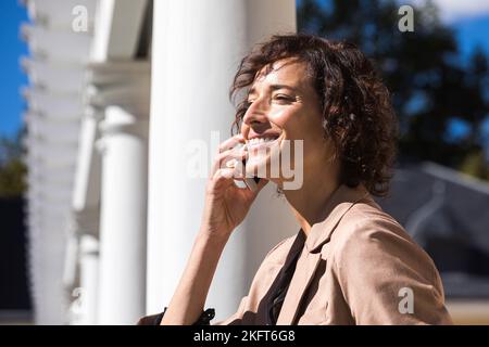 Vue latérale d'une jeune femme d'affaires avec des cheveux bouclés parlant sur un téléphone portable par beau temps Banque D'Images