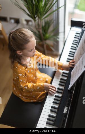 De dessus blonde petite fille pratiquant la musique sur piano dans intérieur lumineux de maison Banque D'Images