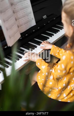 De dessus blonde petite fille pratiquant la musique sur piano dans intérieur lumineux de maison Banque D'Images