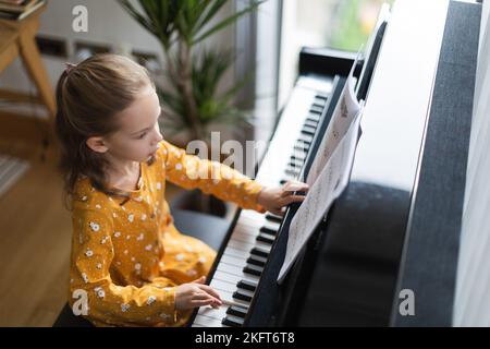 De dessus blonde petite fille pratiquant la musique sur piano dans intérieur lumineux de maison Banque D'Images