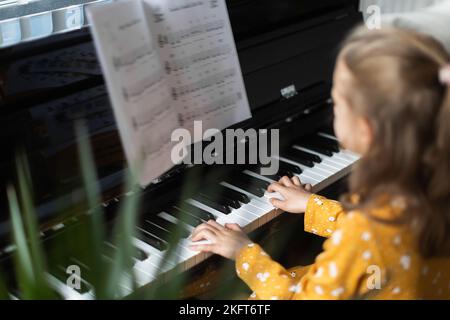 De dessus blonde petite fille pratiquant la musique sur piano dans intérieur lumineux de maison Banque D'Images