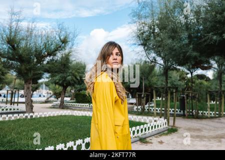 Femme tendance avec des cheveux ondulés donnant loin dans le parc avec de l'herbe verte et des arbres à Donostia de San Sebastian en Espagne Banque D'Images
