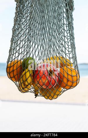 Pommes mûres oranges et bananes placées dans un sac à corde sur fond flou de la plage d'Ondarreta de San Sebastian en Espagne Banque D'Images