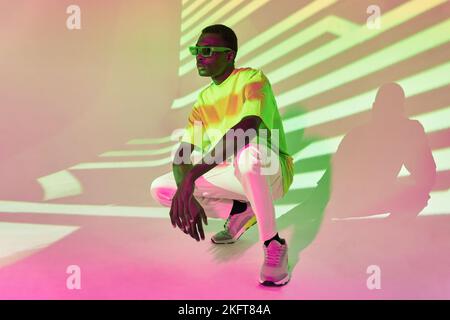Ensemble complet de jeunes Afro-américains en tenue décontractée posant accroupi près du mur avec des ombres rayées dans une lumière vive Banque D'Images