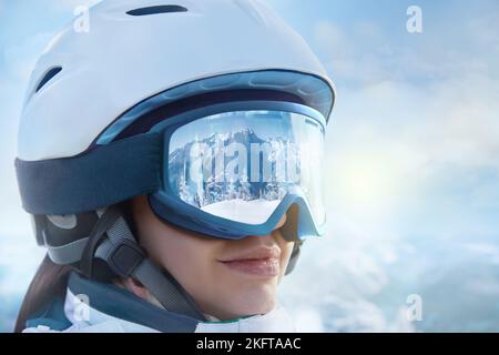 Portrait de la jeune femme à la station de ski sur le fond des montagnes et du ciel bleu.Une chaîne de montagne reflétée dans le masque de ski. Sports d'hiver. Banque D'Images