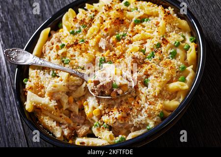 Gros plan de Tpas Mornay, crémeux Thon Casserole Penne Pasta Bake dans un plat à pâtisserie sur une table en bois sombre avec une cuillère Banque D'Images