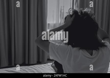 Concept de la Journée mondiale de la santé mentale. Vue arrière de la femme en colère mettre la main sur la tête et tirer les cheveux. Une femme souffrant de maladie mentale s'assoit au lit dans la chambre. Femme Banque D'Images