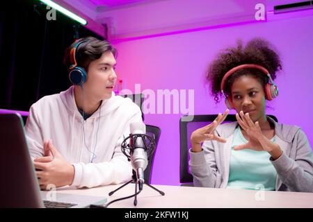 Jeune femme afro-américaine et homme asiatique un podcast interview et conversation ensemble en studio, homme et femme hôte portant casque parler avec Banque D'Images