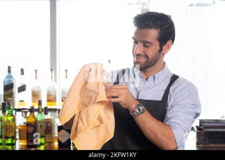 Le jeune homme caucasien est barman de nettoyage et d'essuyer le verre avec professionnel au comptoir, portrait beau mâle de préparation verre ou de wineglass, barman s. Banque D'Images