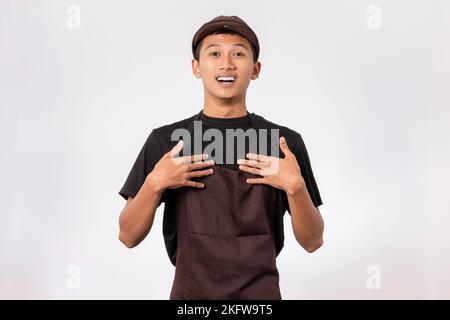 Beau barista asiatique portant un tablier marron et un t-shirt noir isolé sur fond blanc choqué par la surprise et l'expression stupéfaite Banque D'Images
