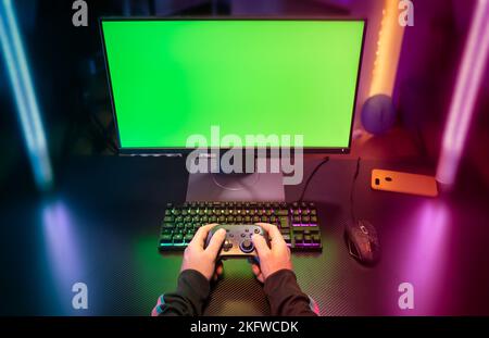 POV des mains de joueur jouant avec le joystick sur écran vert dans la salle à la mode et élégante avec lumière de néon Banque D'Images