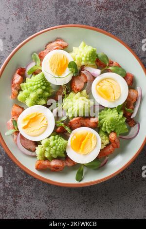 Délicieux petit déjeuner de chou romanesco, œufs durs, bacon frit et micro-légumes dans une assiette sur la table. Vue verticale du dessus Banque D'Images