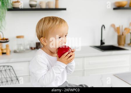 L'enfant mange une pomme pour le petit-déjeuner assis dans la cuisine. Une alimentation saine pour toute la famille Banque D'Images