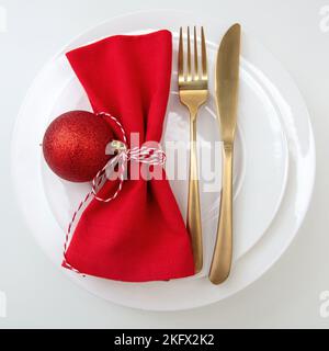 Table de Noël, dîner de fête. Coutellerie dorée et serviette en tissu rouge sur des assiettes isolées sur blanc, vue du dessus Banque D'Images