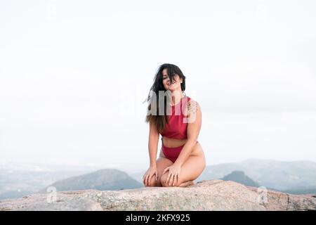 Femme d'âge mûr de race blanche assise sur ses talons avec ses cheveux couvrant son visage souriant regardant l'appareil photo du grand rocher Banque D'Images