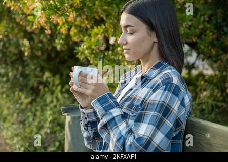 Fille assise sur un banc buvant un café avec des arbres en arrière-plan Banque D'Images