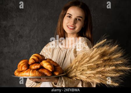 Femme ukrainienne vêtue d'une robe nationale tient un plateau avec des croissants roses sur un fond sombre Banque D'Images