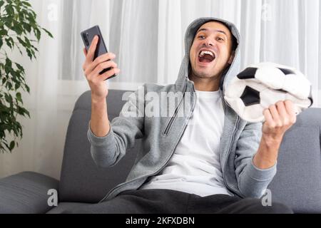 fan de football choqué dans un t-shirt bleu avec smartphone et tenant le ballon de football Banque D'Images