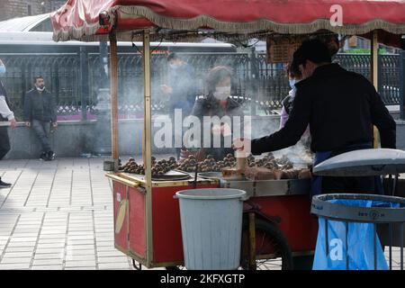 Une femme âgée avec un masque achetant des châtaignes d'un vendeur de rue en hiver Banque D'Images