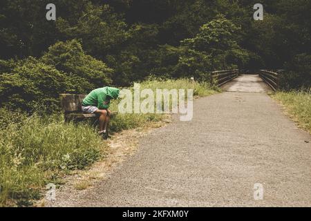 Homme assis sur un chemin au milieu de la nature avec une attitude dépressive. Concept de désordre émotionnel. Banque D'Images