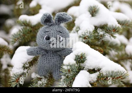 Lapin tricoté gris sur une branche de sapin recouvert de neige. Symbole du nouvel an chinois 2023 Banque D'Images