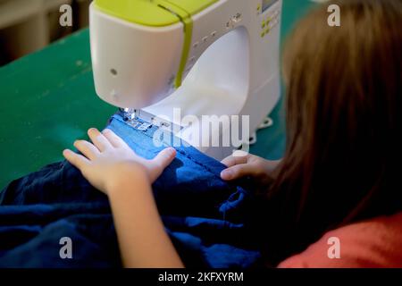 Les mains d'une jeune fille qui se coud sur une machine à coudre. Le concept de petite entreprise, passe-temps, loisirs à la maison. ECO, zéro déchet, recyclage. Banque D'Images