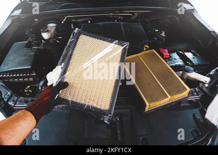 Un mécanicien d'automobiles possède un filtre à air neuf enveloppé dans du plastique et un moteur de véhicule qui a un ancien filtre à air sale. Banque D'Images