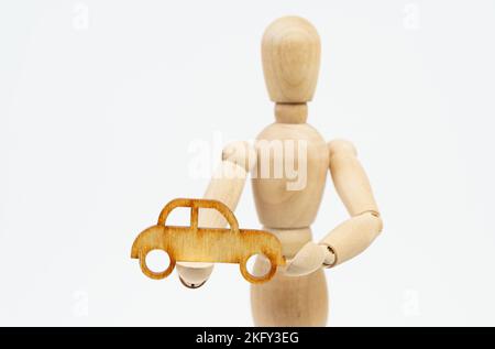 Concept d'entreprise. L'homme en bois tient une voiture de tourisme dans ses mains. Isolé sur fond blanc. Banque D'Images