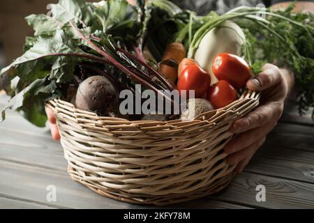 Mains d'homme méconnaissables tenant un panier en osier avec récolte de légumes frais d'oignon, de verdure, de tomate, de betterave, de carotte, moelle. Production agricole Banque D'Images