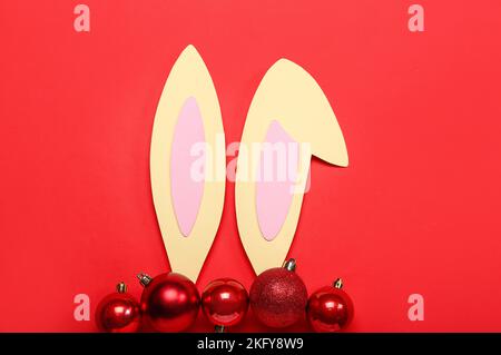 Oreilles de lapin en papier avec boules de Noël sur fond rouge Banque D'Images