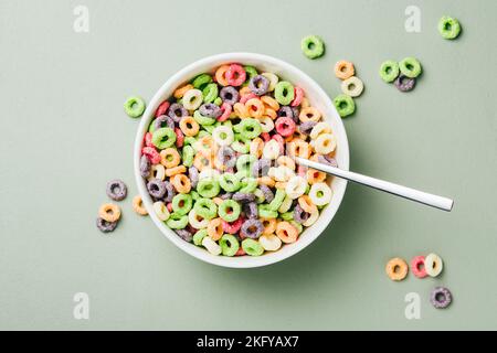 Anneaux de maïs colorés dans un bol sur fond vert. Céréales de petit déjeuner sucrées en forme d'anneau avec lait. Banque D'Images