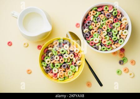 Anneaux de maïs colorés dans un bol sur fond jaune. Céréales de petit déjeuner sucrées en forme d'anneau avec lait. Banque D'Images