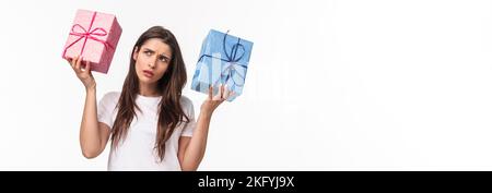 Célébration, fêtes et cadeaux concept. Hmmm intéressant ce qui à l'intérieur. Portrait de curieux jeune fille d'anniversaire secouant des boîtes-cadeaux essayant de Banque D'Images