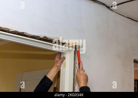 Il y a un ouvrier de garniture utilisant un marteau pendant l'installation des portes intérieures à l'intérieur de la maison neuve Banque D'Images