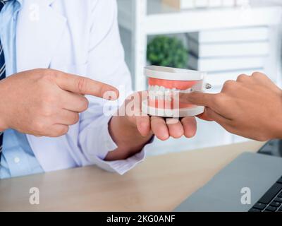 Gros plan d'un modèle de dent dans la main de dentiste. Dentiste mâle présentant une prothèse dentaire propre examinant le diagnostic de l'hygiène dentaire de la jeune femme en clinique médicale Banque D'Images