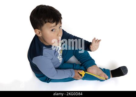 Enfant d'environ 4 ans vêtu de vêtements d'hiver, allongé sur le sol mesurant un pied avec un mètre ruban. Banque D'Images