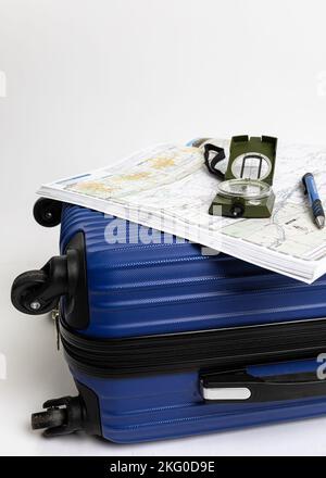 Une valise de voyage bleue s'affiche à côté des cartes, de la boussole et du stylet, le tout sur un fond blanc Banque D'Images