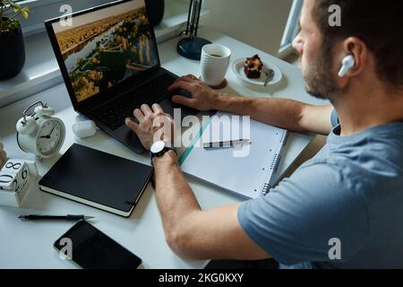 Indépendant travaillant au bureau à domicile. Homme utilisant un ordinateur portable et écrivant dans le bloc-notes assis à une table dans le bureau à la maison Banque D'Images
